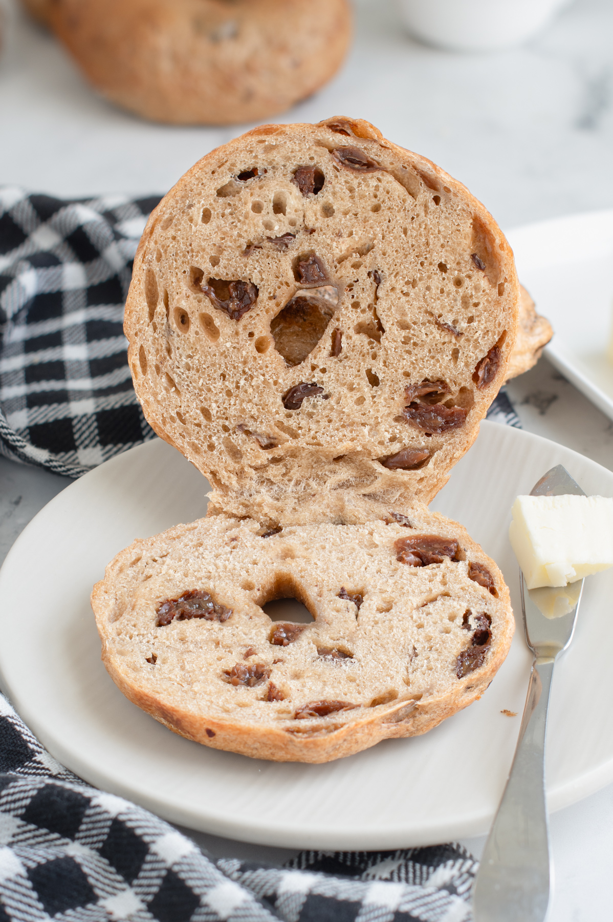 a cut sourdough cinnamon raisin bagel on a white plate.