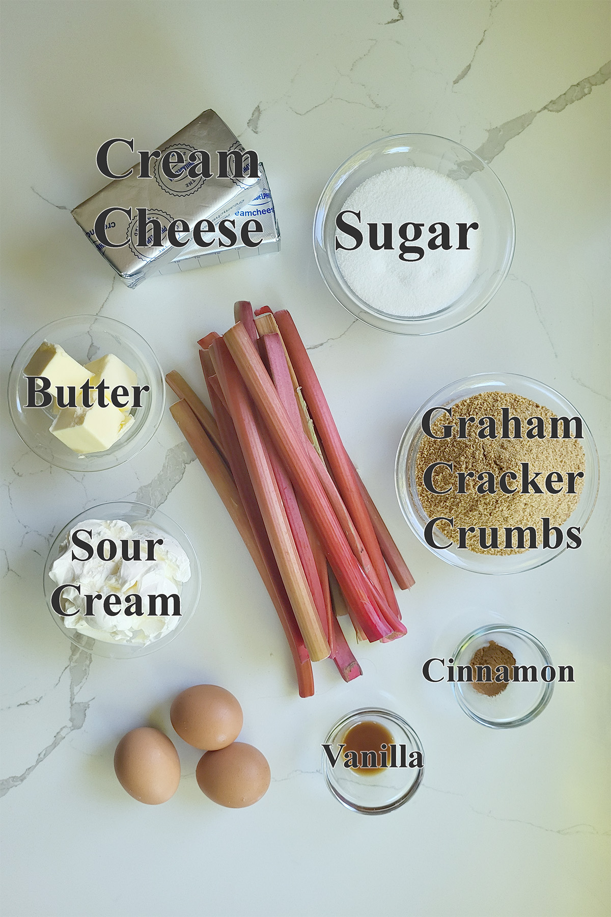 ingredients for rhubarb cheesecake in glass bowls on a white surface.