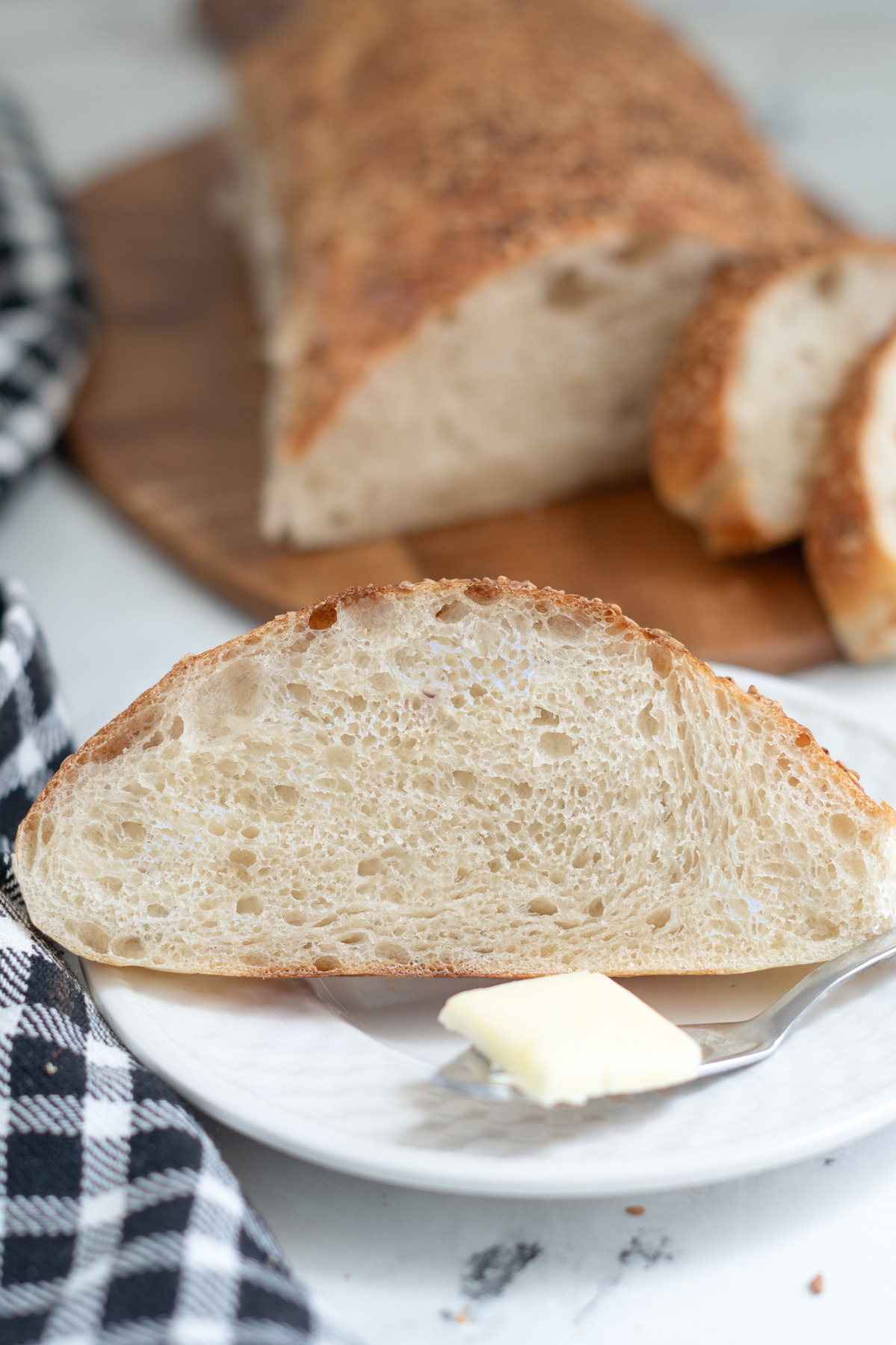 a slice of sourdough italian bread on a white plate with a knife and butter pat.