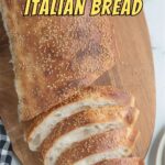a loaf of italian bread, partially sliced, on a cutting board.