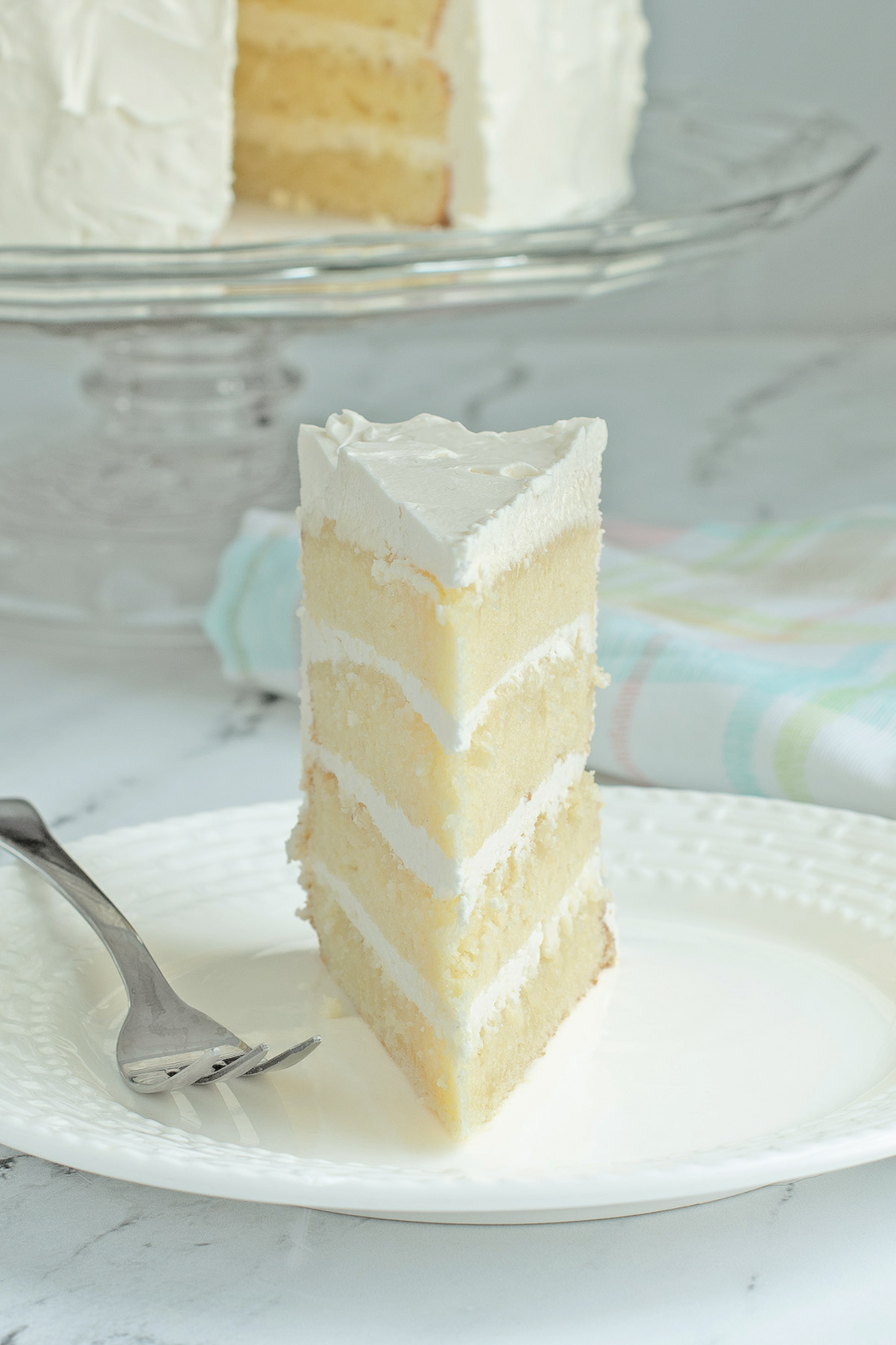 a slice of flour layer vanilla cake on a white plate with a fork.