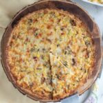 a corn quiche on a wooden cutting board with a slice removed.