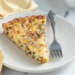 a slice of corn quiche on a white plate with a fork.