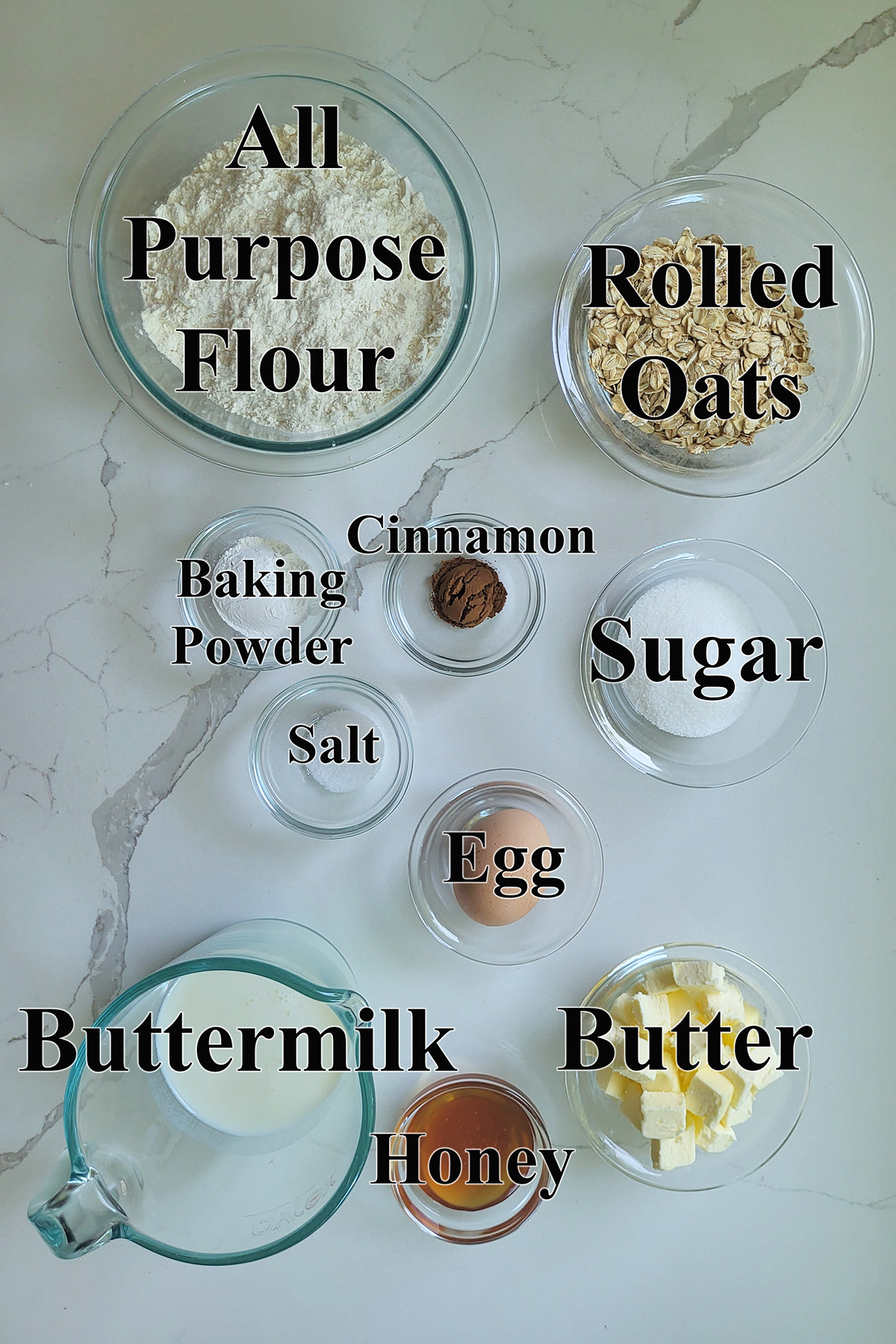 ingredients for oatmeal scones in glass bowls on a marble surface. 