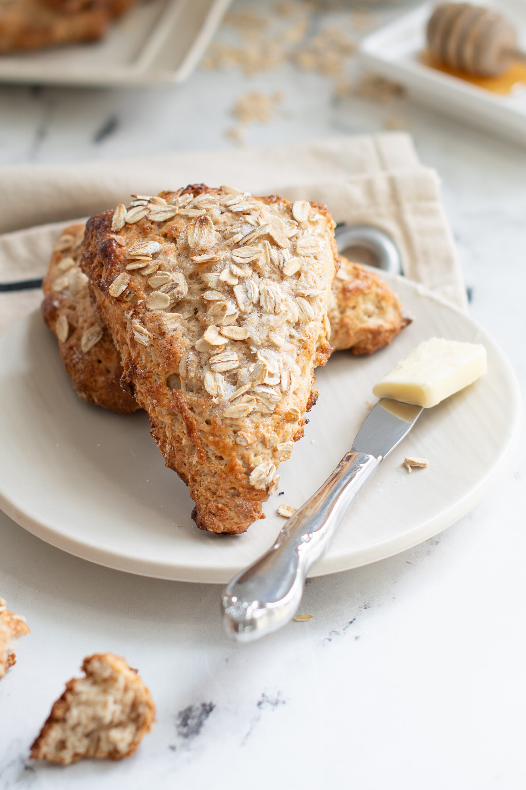 two oatmeal scones on a white plate with a knife and pat of butter. 