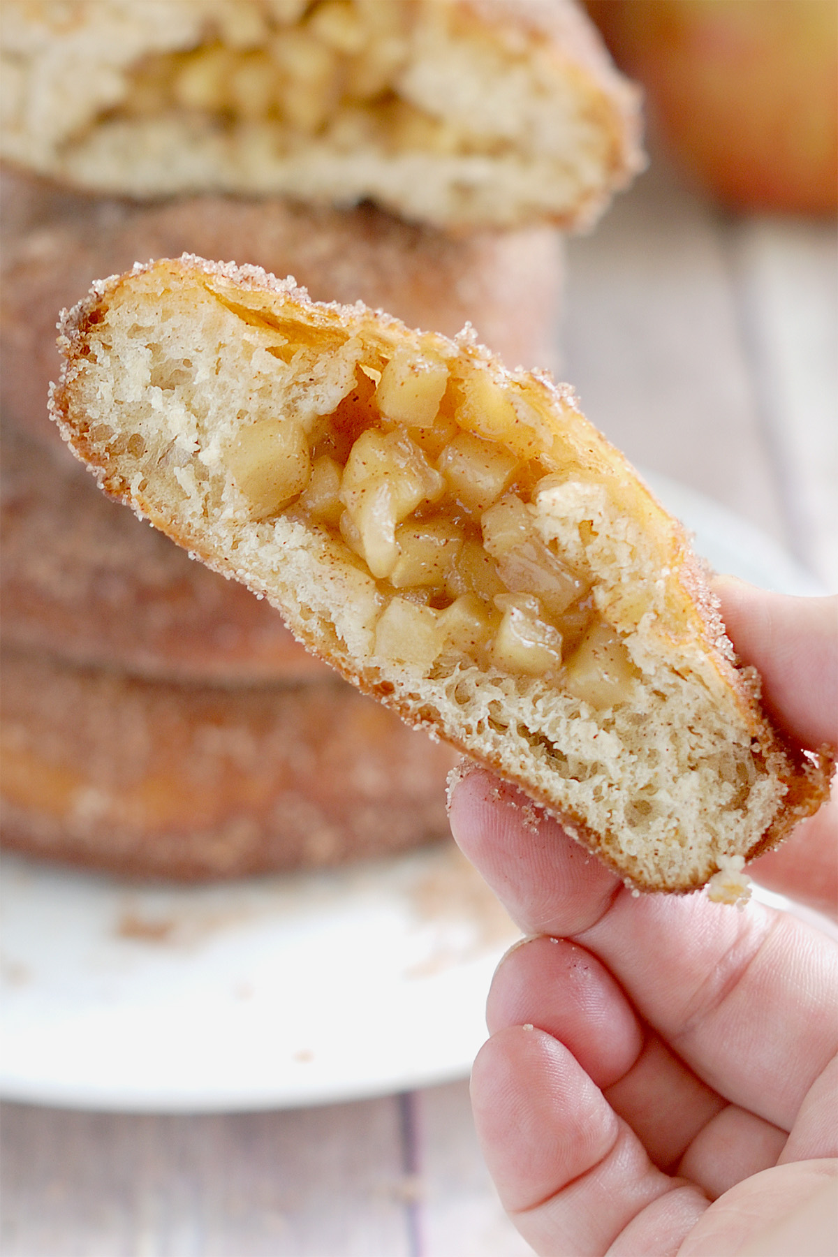 a hand holding a slice apple filled donut, showing the filling.
