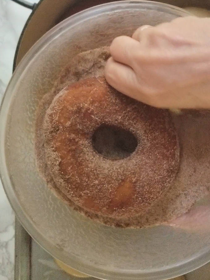 a cider donut being tossed in cinnamon sugar. 