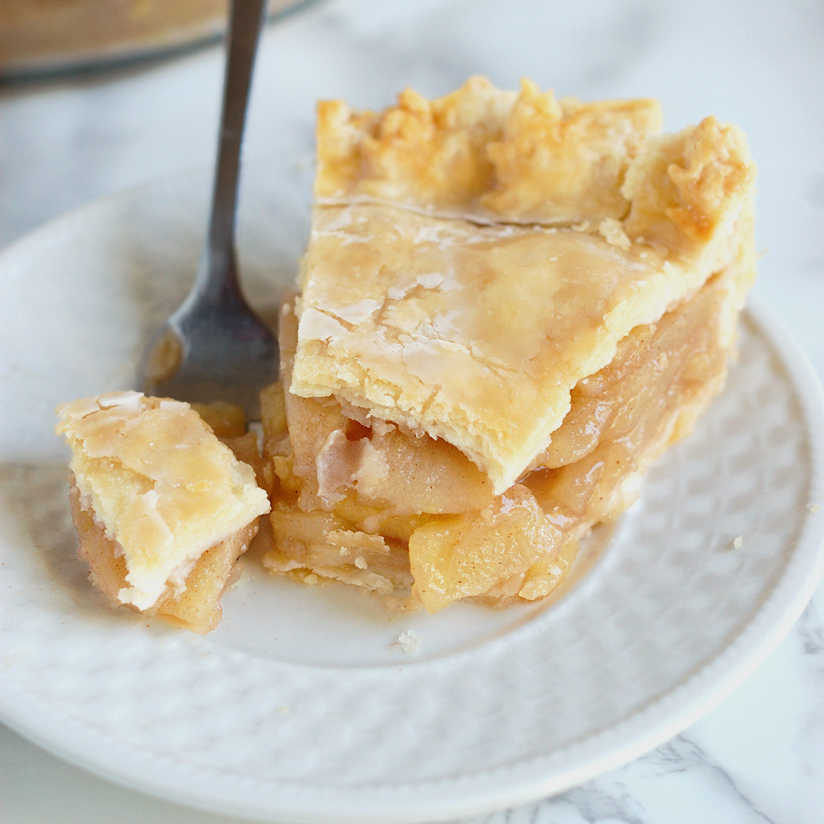 a slice of maple apple pie with a fork on a white plate.