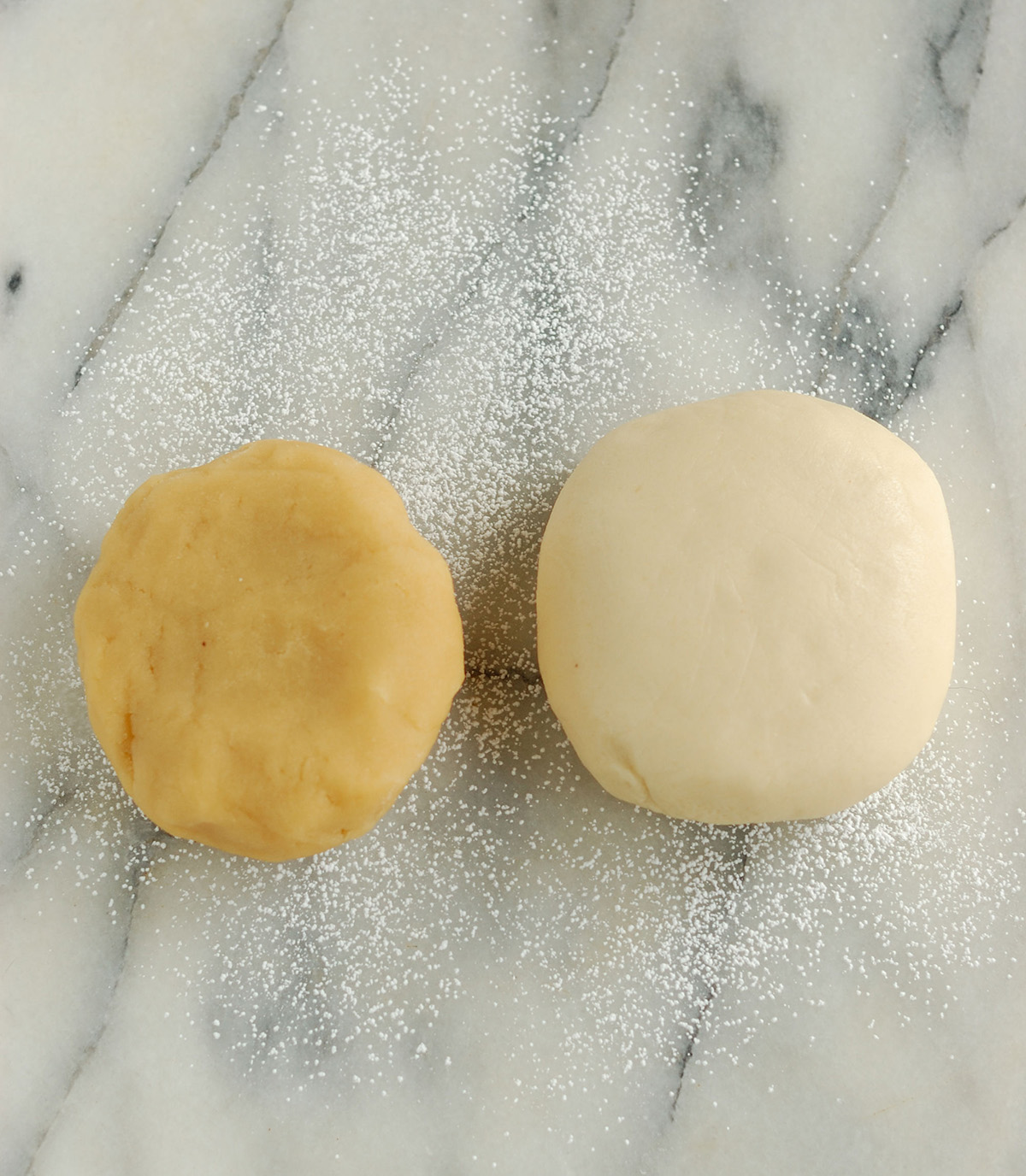 a ball of almond paste and a ball of marzipan next to each other on a marble table.