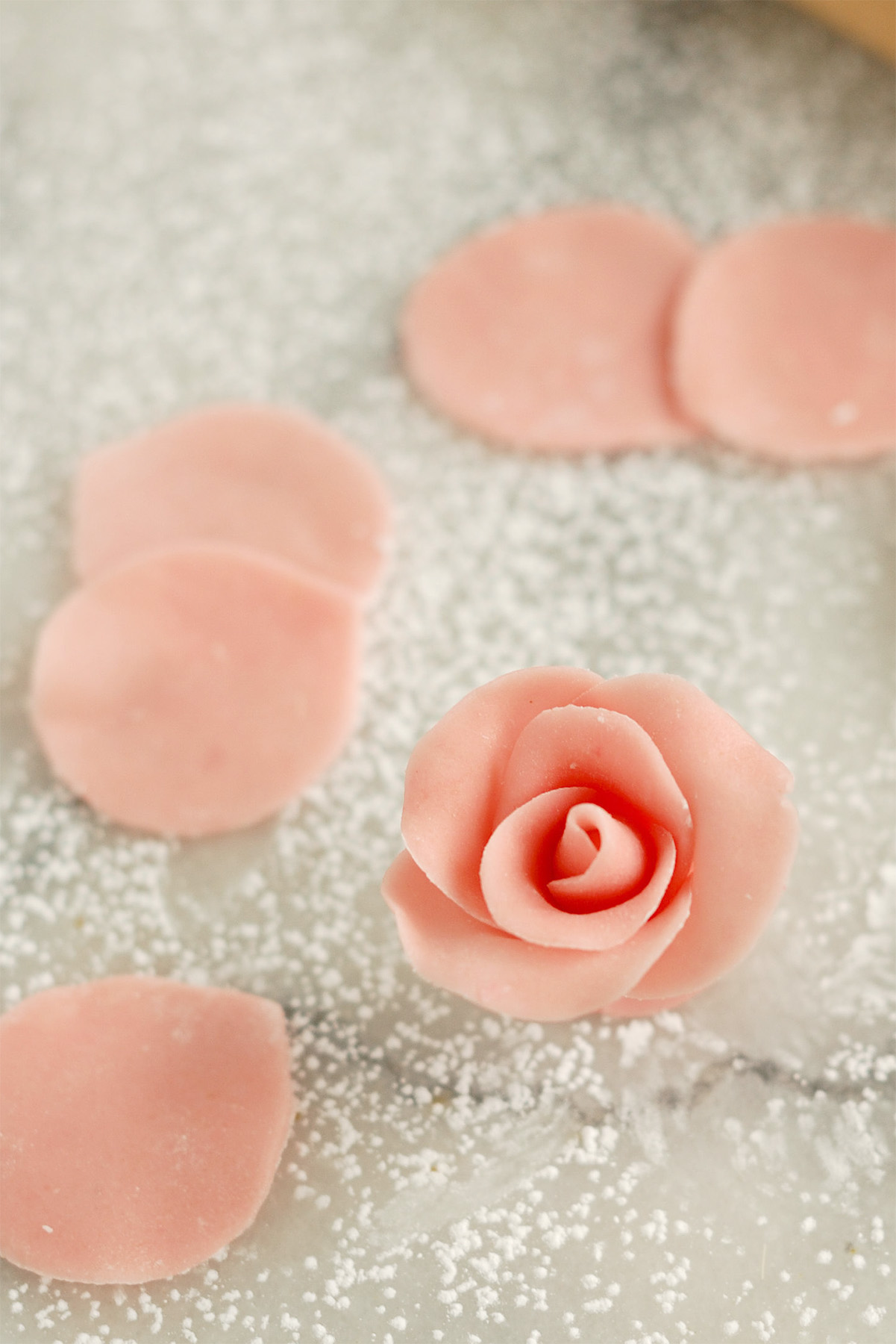 a pink marzipan rose and several pink marzipan rose petals on a marble table.
