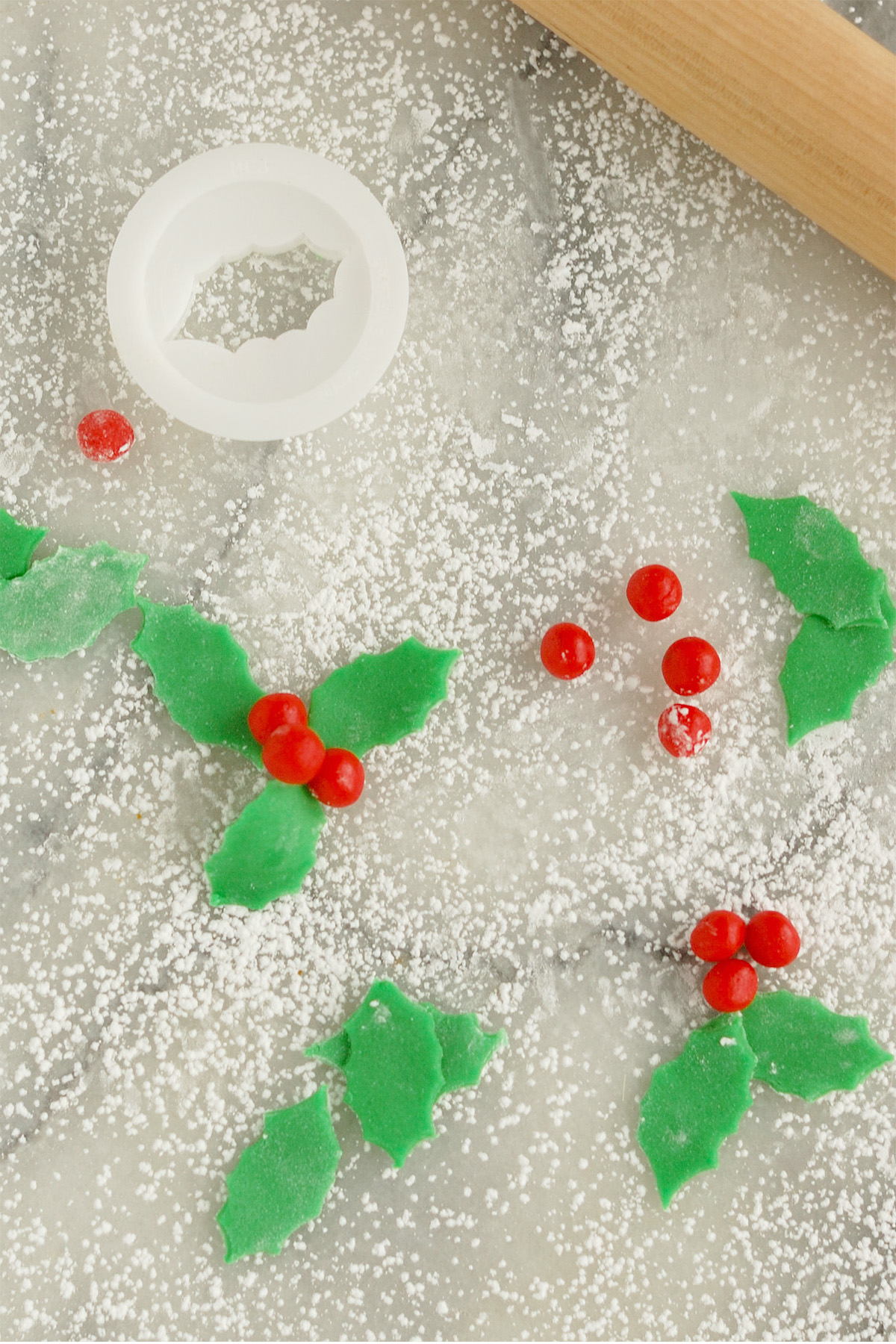marzipan holly leaves and berries sprinkles with powdered sugar on a marble surface. 