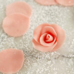 a pink marzipan rose and several marzipan rose petals on a marble table.