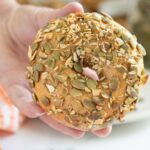 a hand holding a seeded pumpkin bagel.