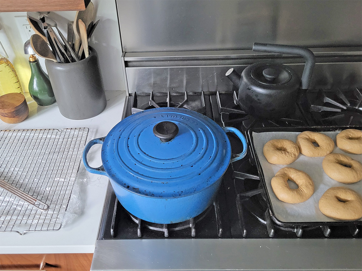 a baking rack on a counter, a blue pot on a stove next to a tray of pumpkin bagels.