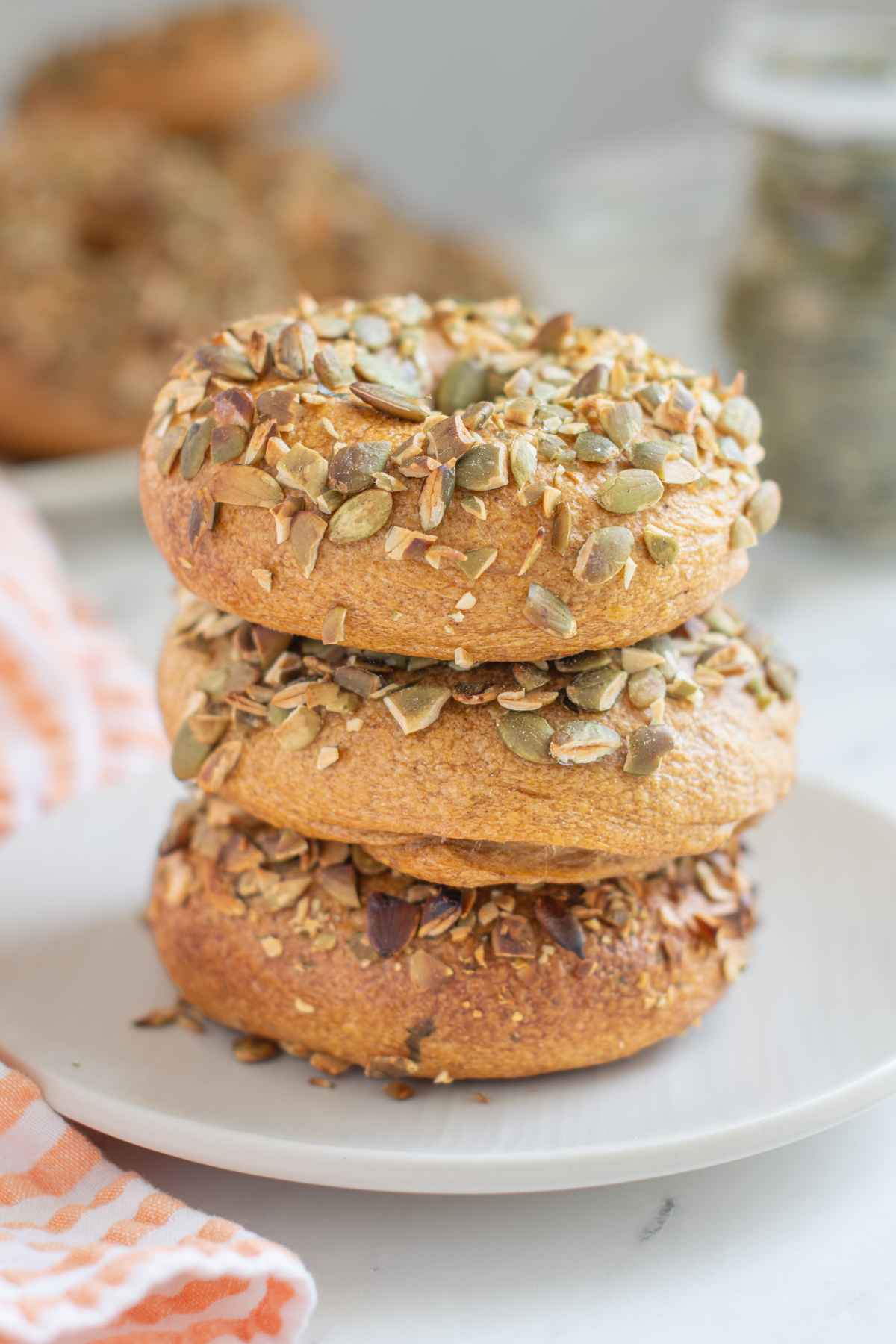 three pumpkin bagels stacked on a white plate.