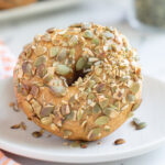a seed covered pumpkin bagel on a white plate.