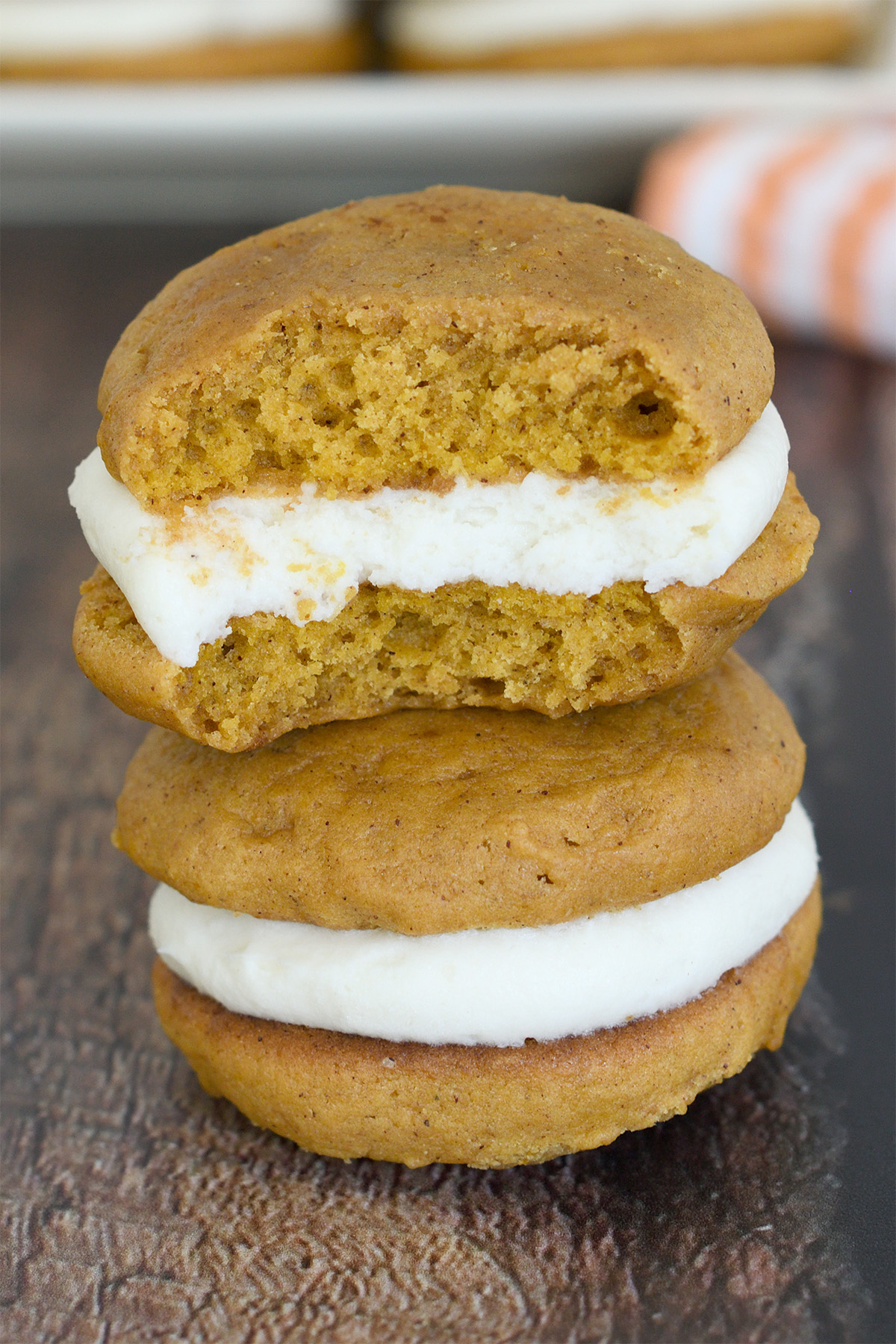 a whole and a bitten pumpkin whoopie pie on a wood table. 