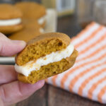 a hand holding a bitten pumpkin whoopie pie.