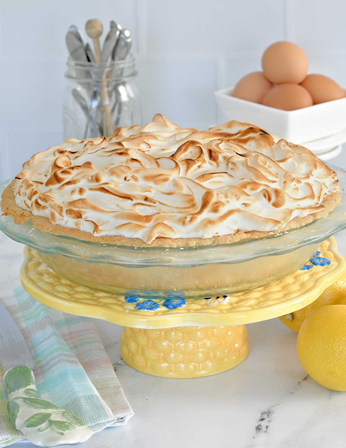 a lemon meringue pie on a yellow cake stand.
