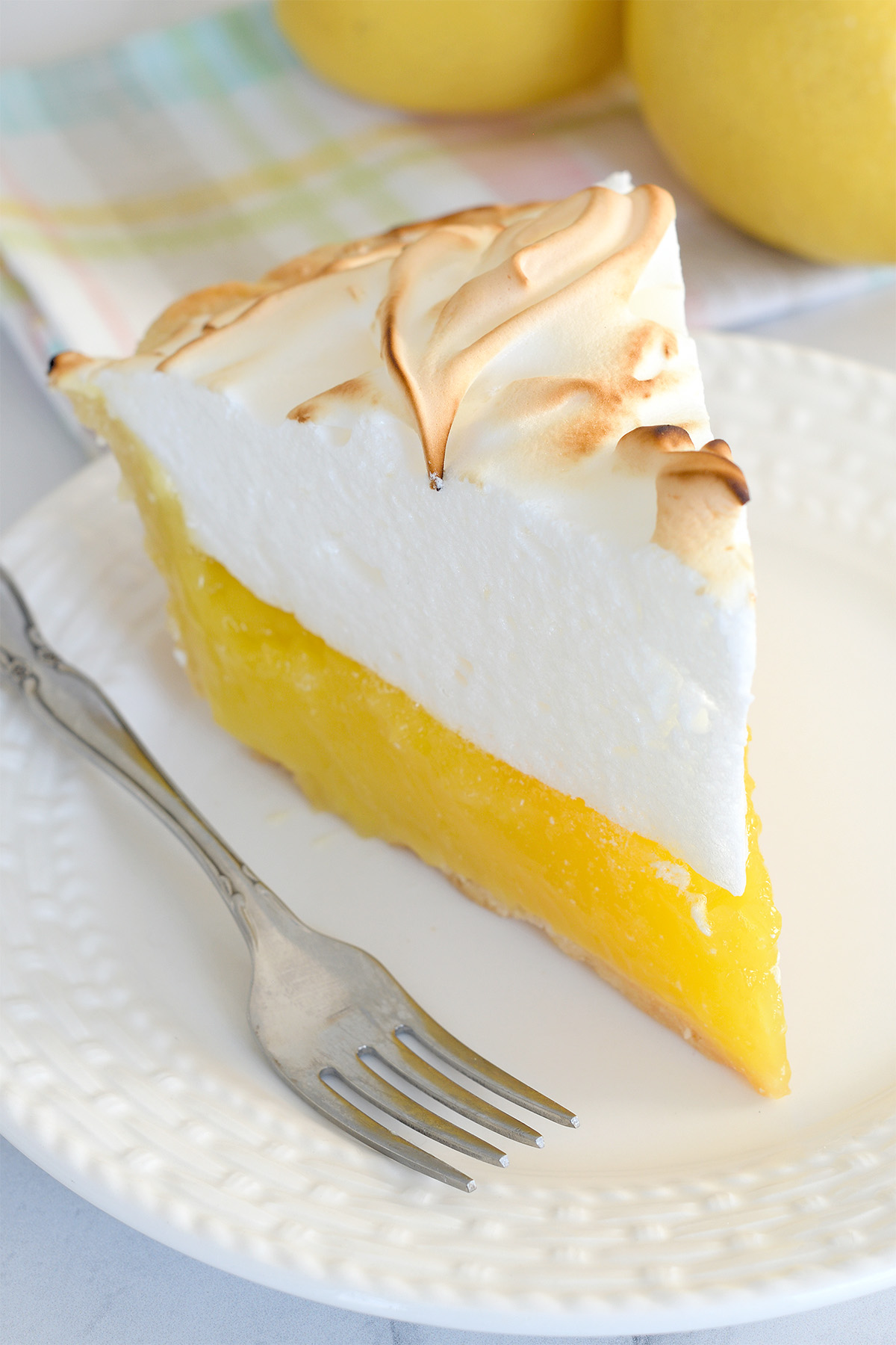 a slice of lemon meringue pie on a white plate with a fork.