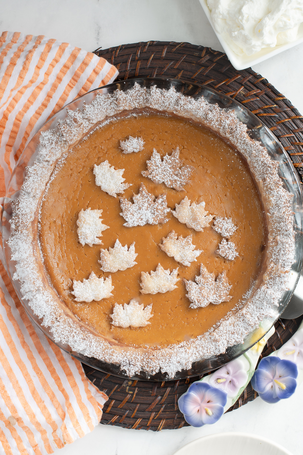a pumpkin pie with leaf cutouts on top on a table with orange striped towel.