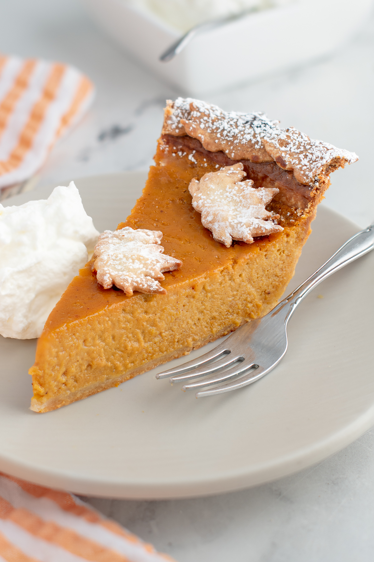 a slice of pumpkin pie with leaf decorations on a white plate.