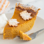 a slice of pumpkin pie with a fork on a white plate.
